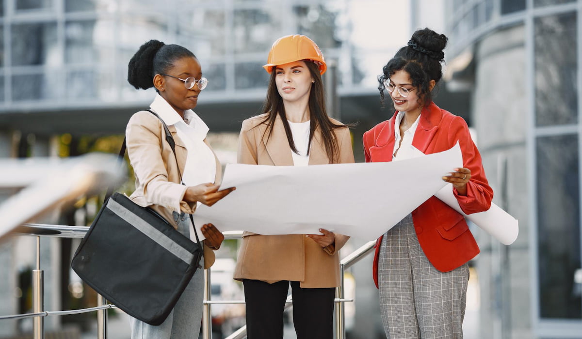 Três mulheres trabalhando como arquitetas em uma construção e tomando uma decisão sobre a planta de um edifício